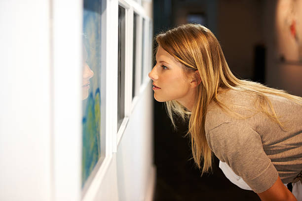 A young woman leaning over and closely examining a painting